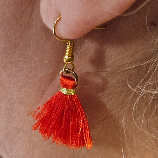 Close-up of a red tassel earring on an ear with a blurred background