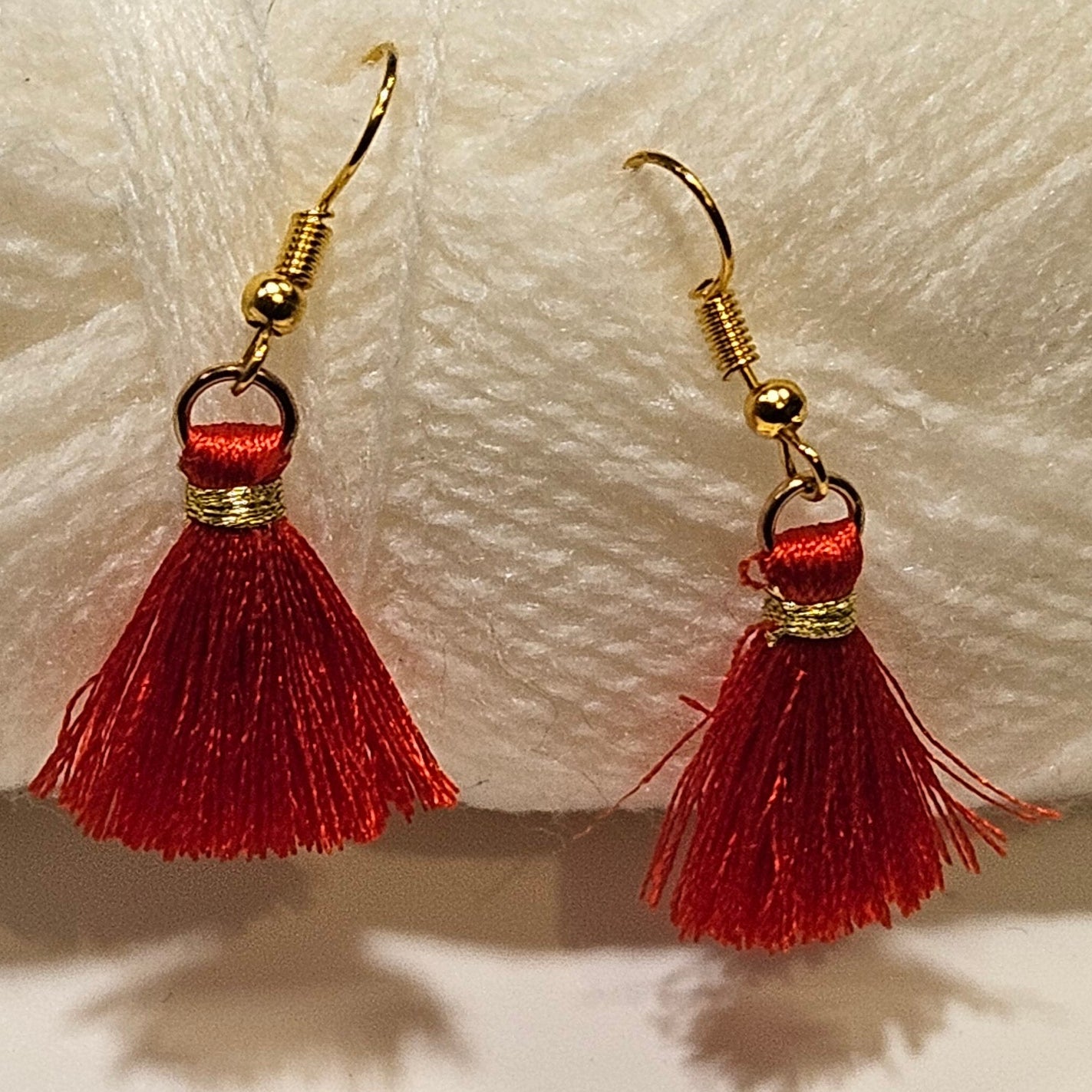 Red tassel earrings with gold accents on a white yarn ball