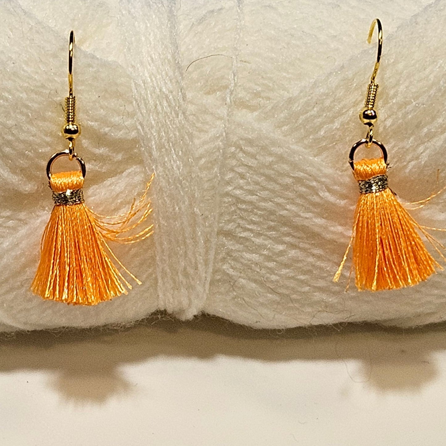 Pair of gold earrings with orange tassels in front of a ball of white yarn.