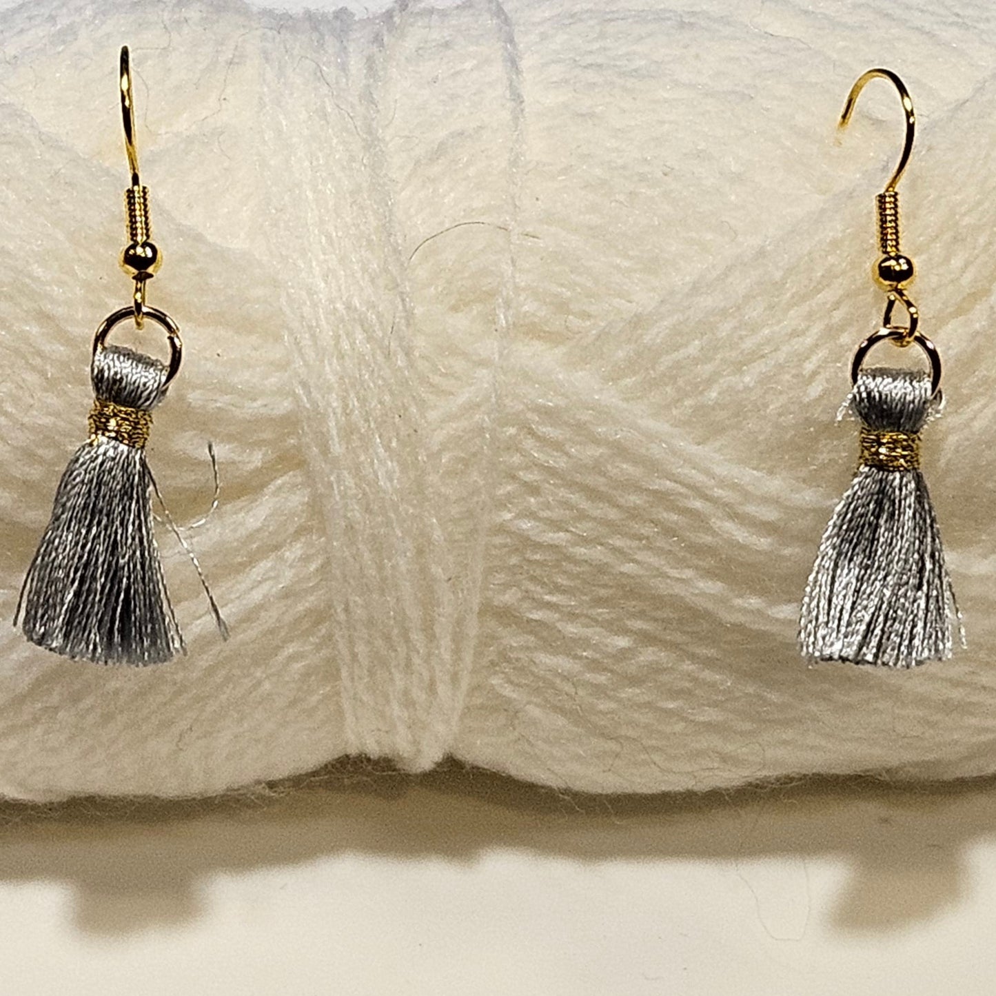 White yarn ball with silver tassel earrings on a light gray background
