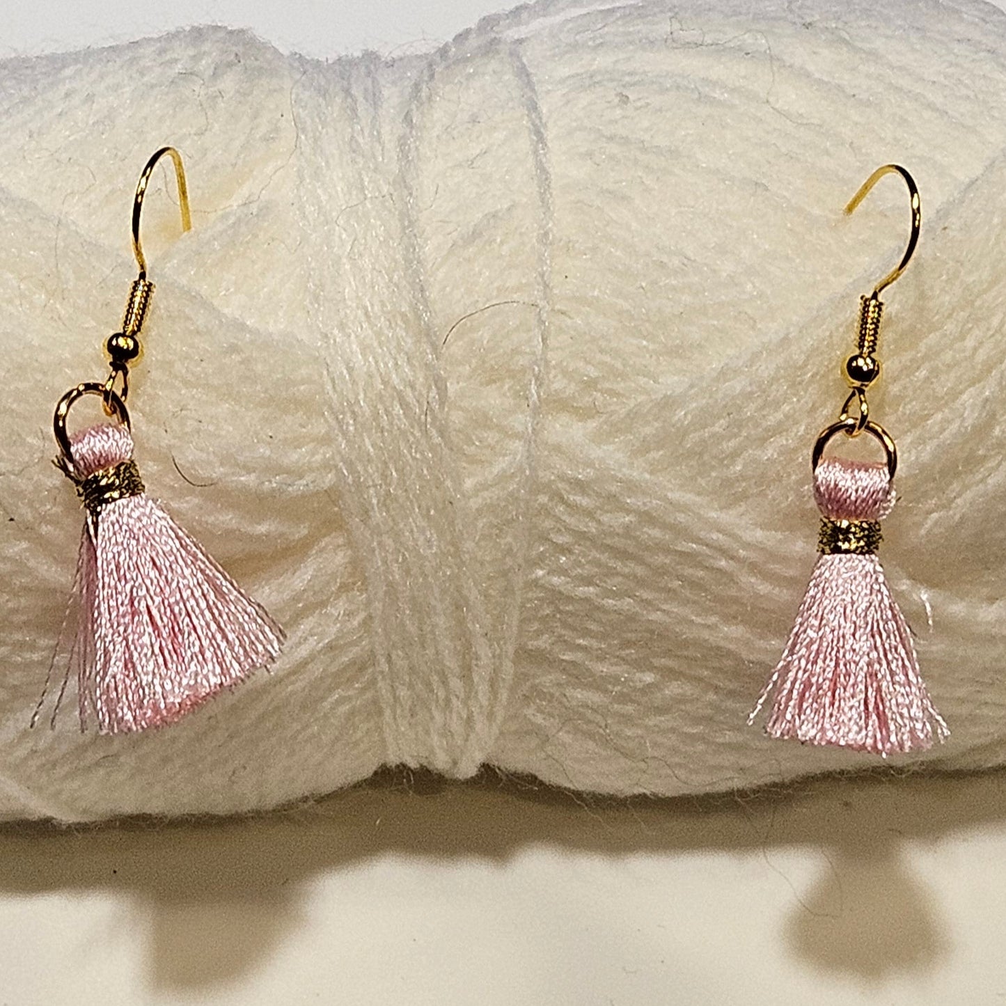 Pair of pink tassel earrings on a ball of white yarn.
