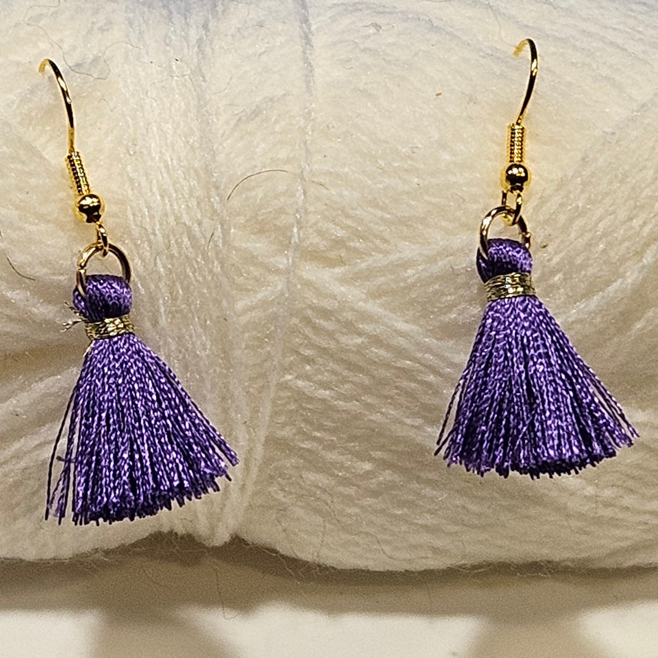 Purple tassel earrings in front of a ball of white yarn on a light gray background