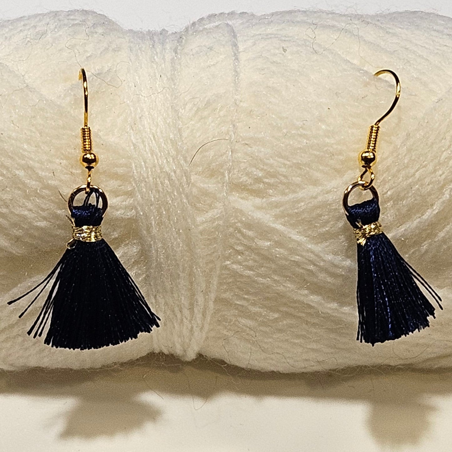 Black tassel earrings with gold accents on a ball of white yarn.