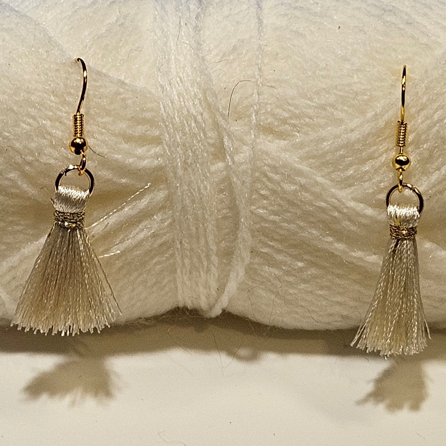 Cream-colored yarn skein with tassel earrings on a white background