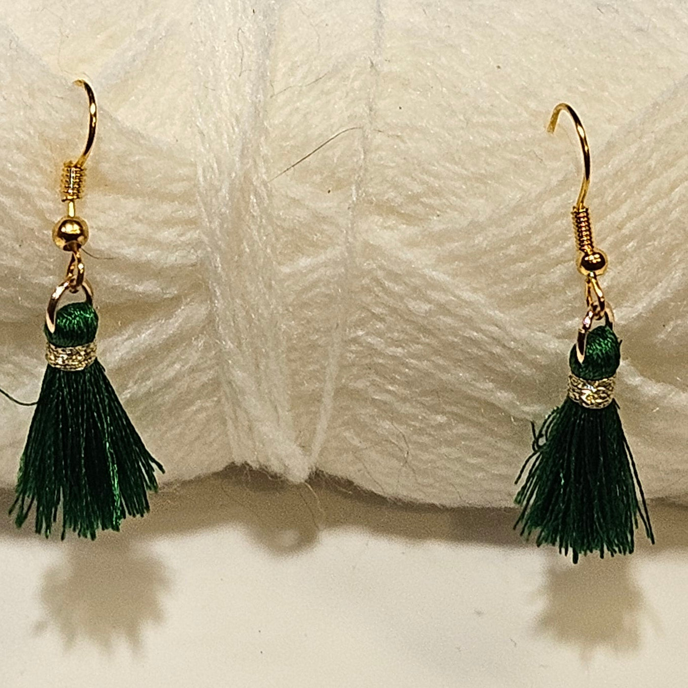 Green tassel earrings in front of a ball of white yarn on a light gray background