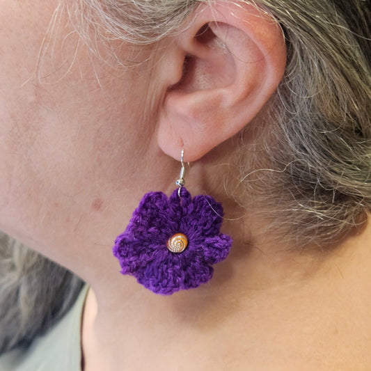 Purple crocheted flower earring worn by a person with gray hair.