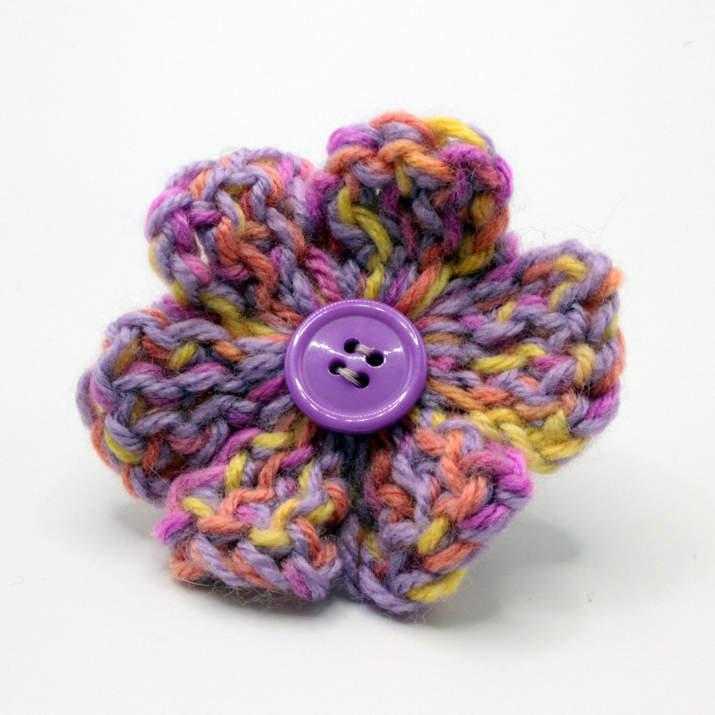 Colorful knitted flower with a purple button in the center on a white background