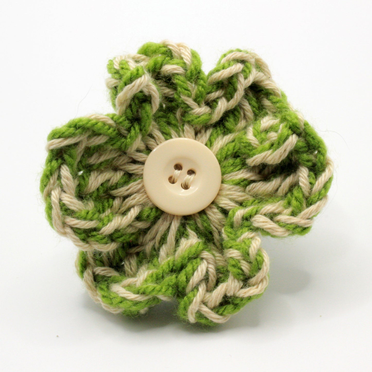 Green and beige knitted flower with a button center on a white background