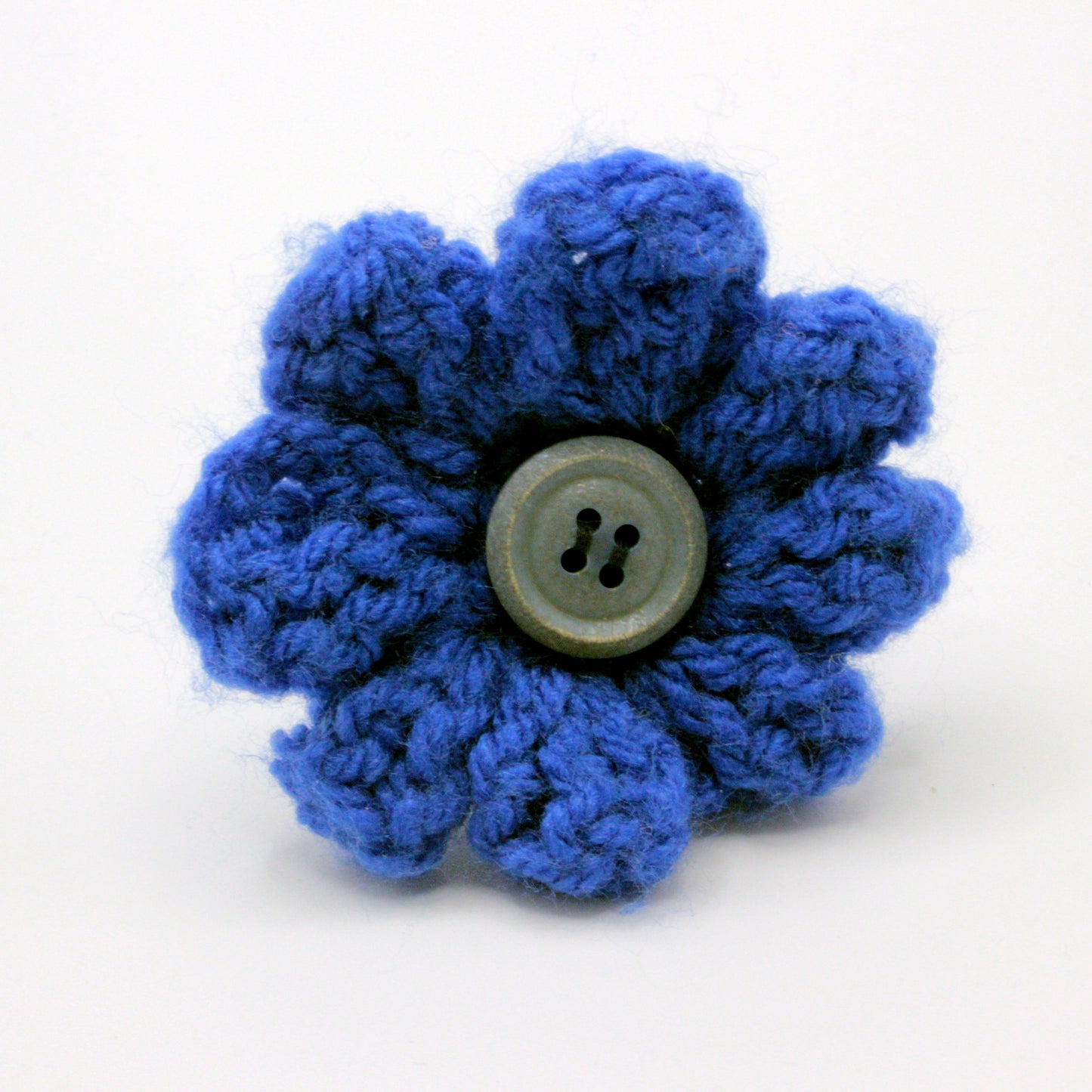 Blue knitted flower with a central button on a white background