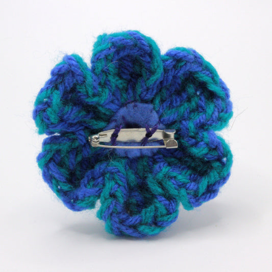 Blue and green crocheted flower with a barrette on a white background