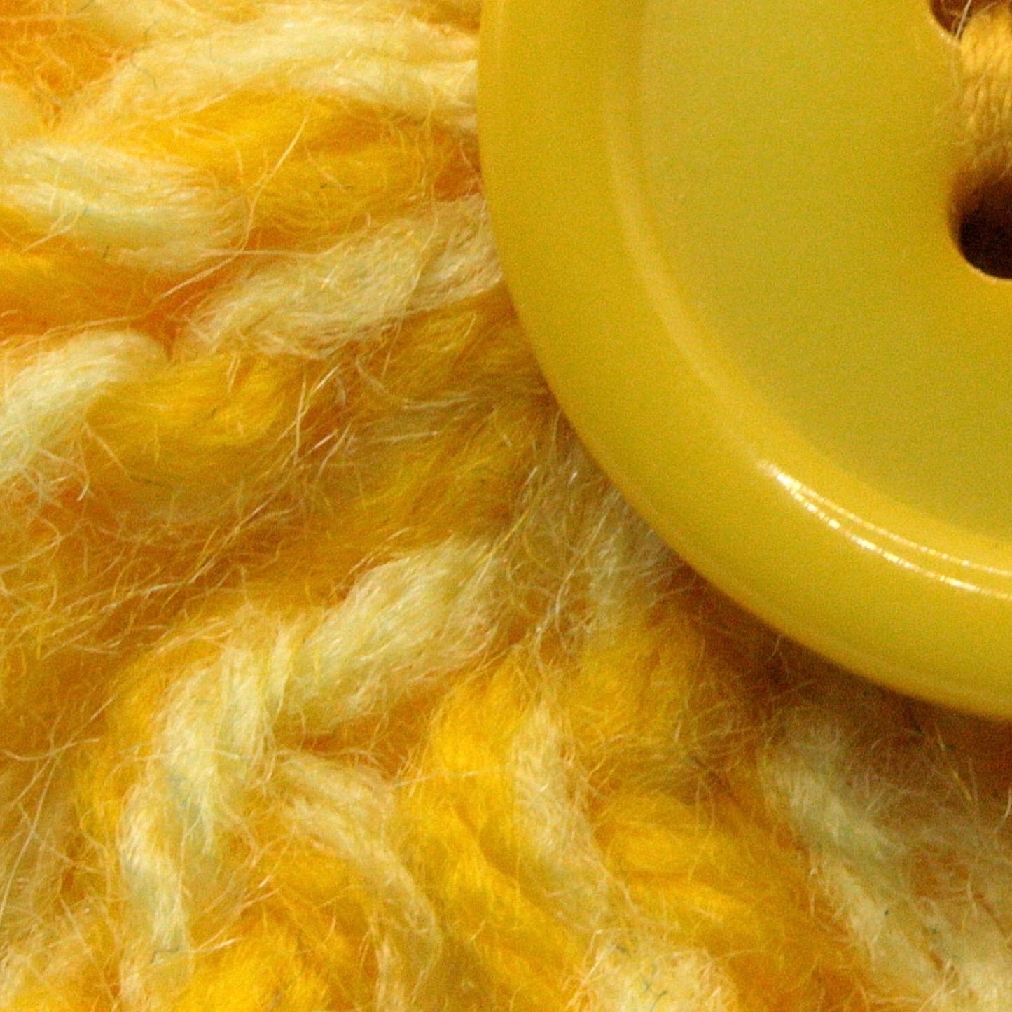 Close-up of yellow yarn and a yellow button on a textured yellow background