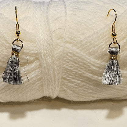 White yarn ball with silver tassel earrings on a light gray background