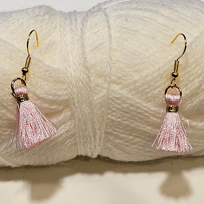 Pair of pink tassel earrings on a ball of white yarn.