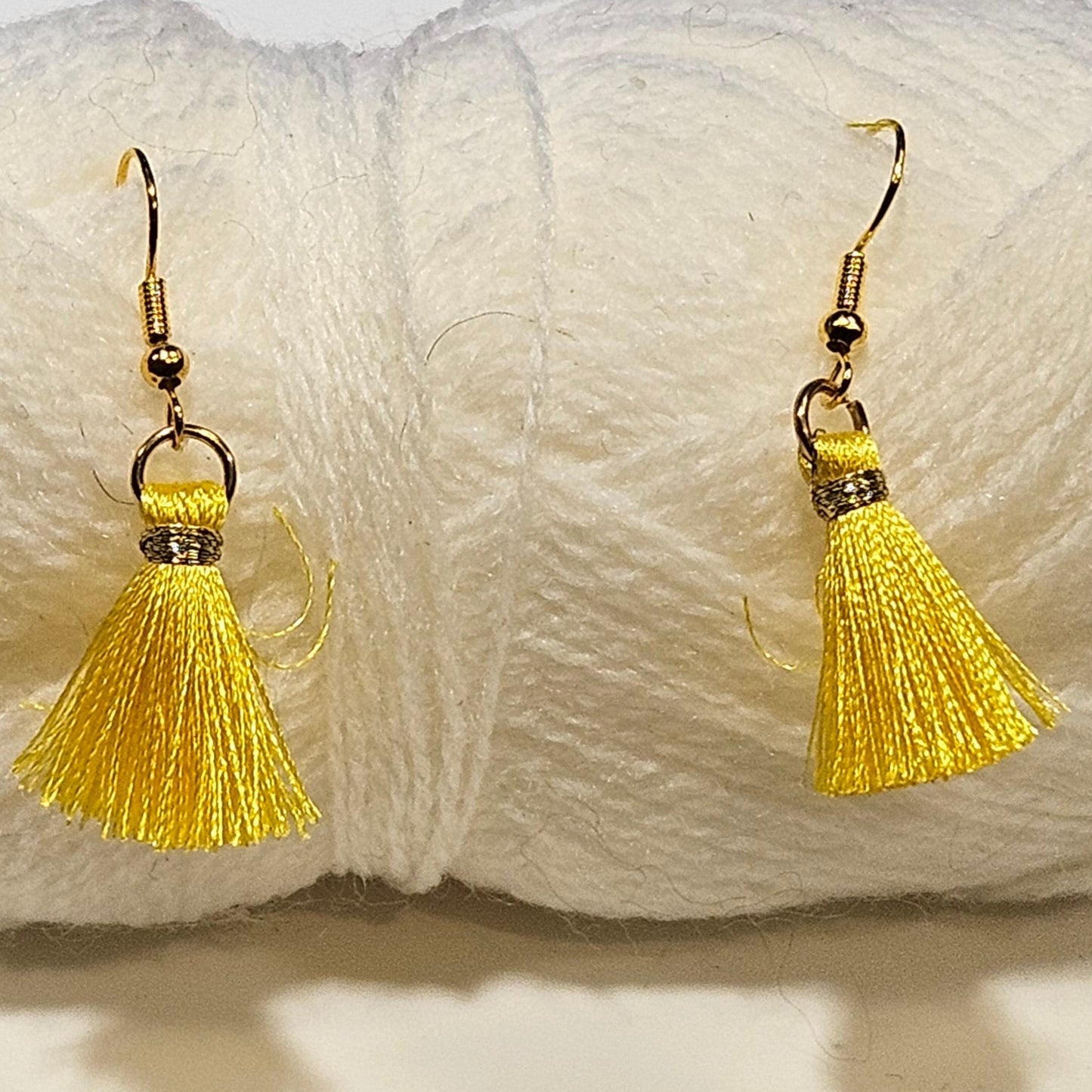Yellow tassel earrings in front of a ball of white yarn on a light gray background