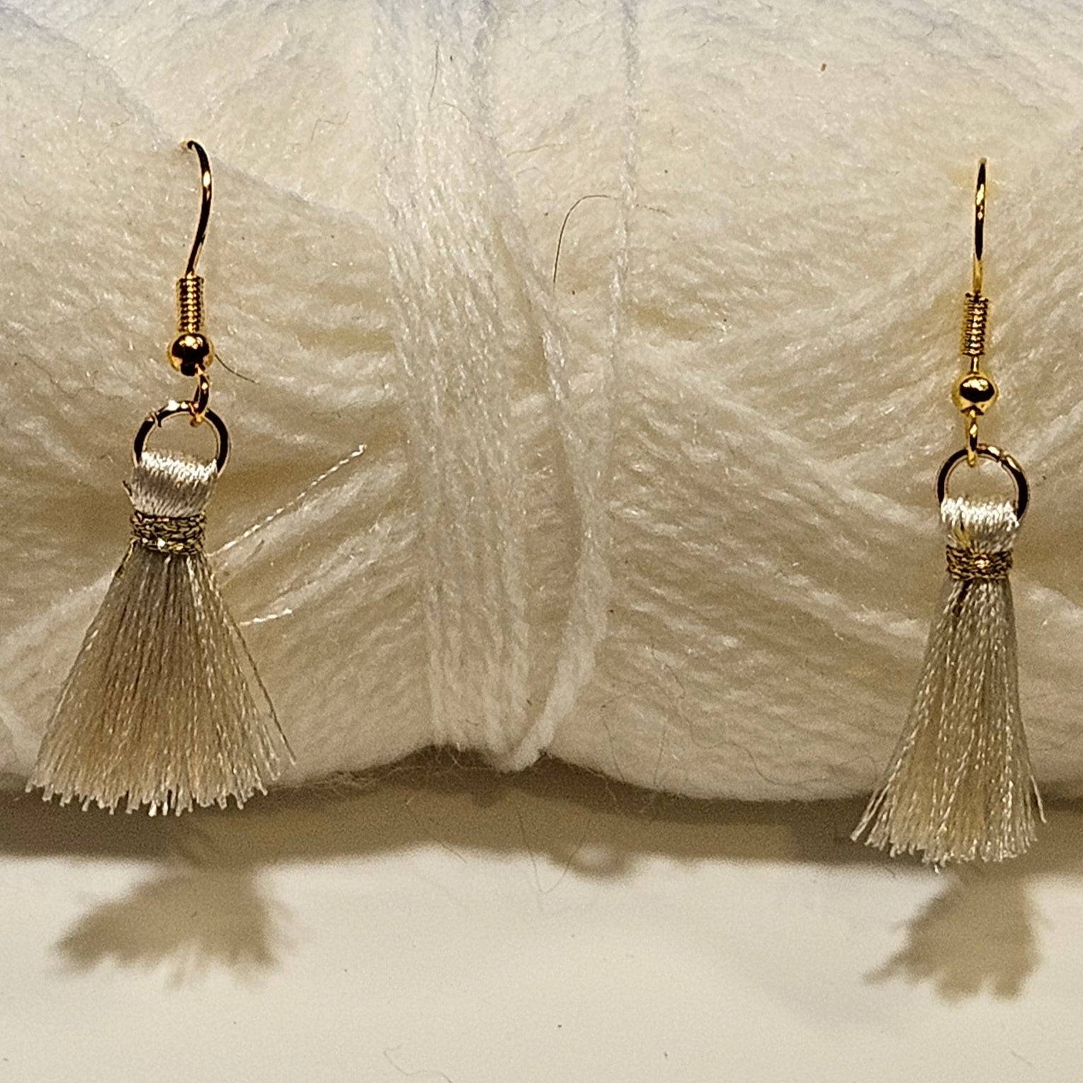 Cream-colored yarn skein with tassel earrings on a white background