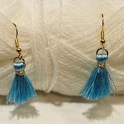 Blue tassel earrings in front of a ball of white yarn on a light gray background