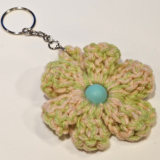 Crocheted flower keychain with a blue button center on a white background