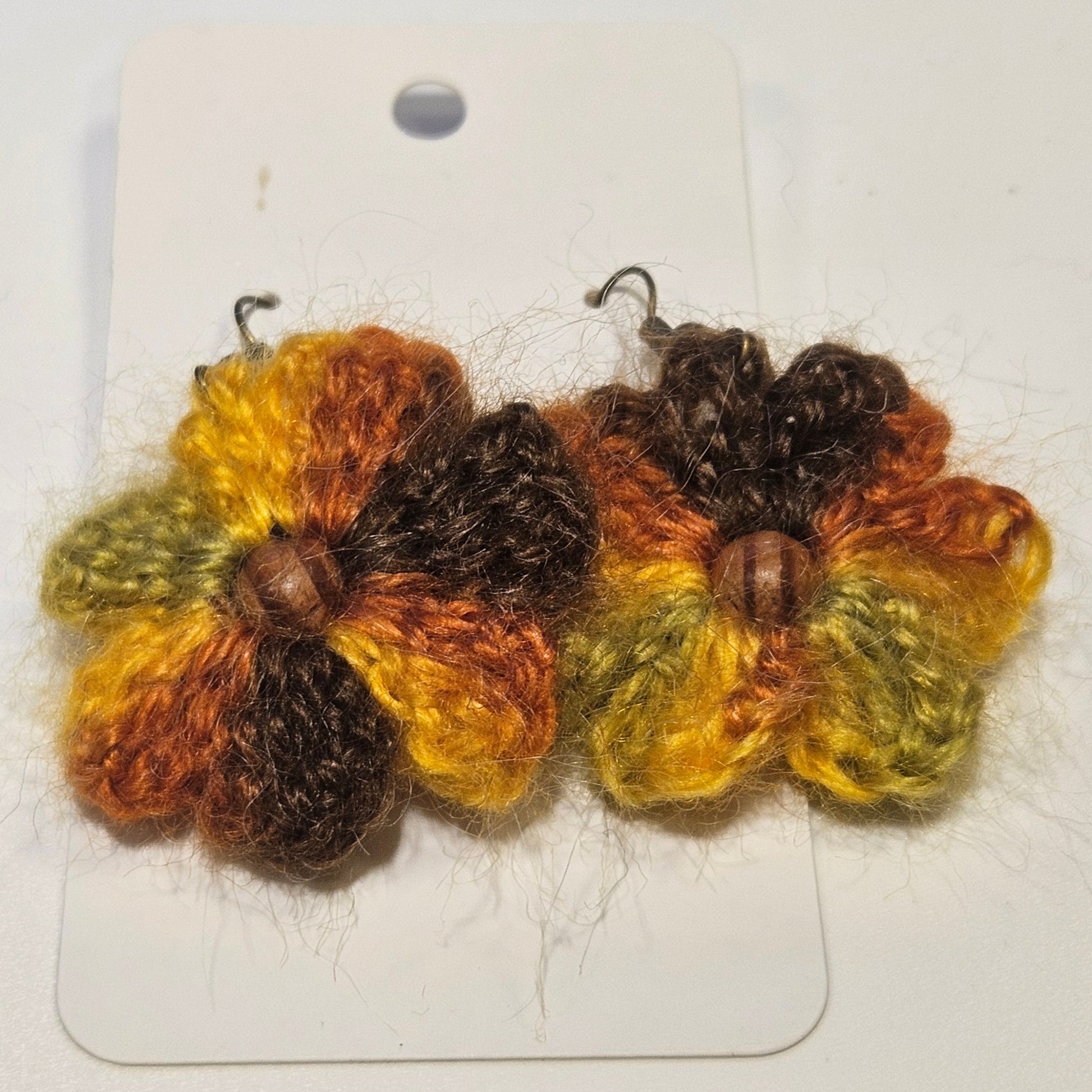 Pair of knitted flower earrings on a white card with a beige background