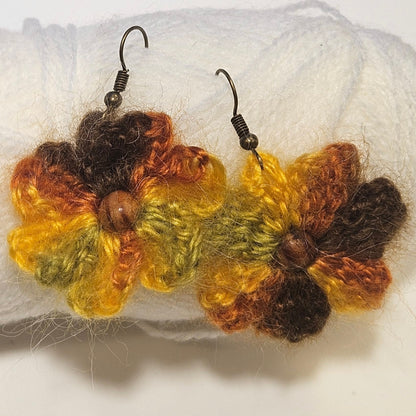 Pair of crocheted flower earrings on a ball of yarn against a white background