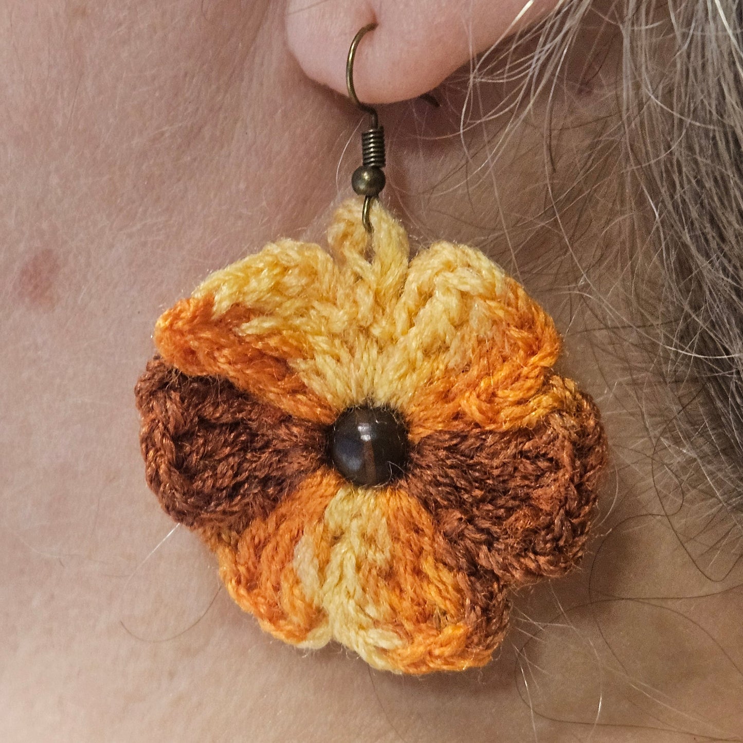 Crocheted flower earring worn on an ear with a neutral background