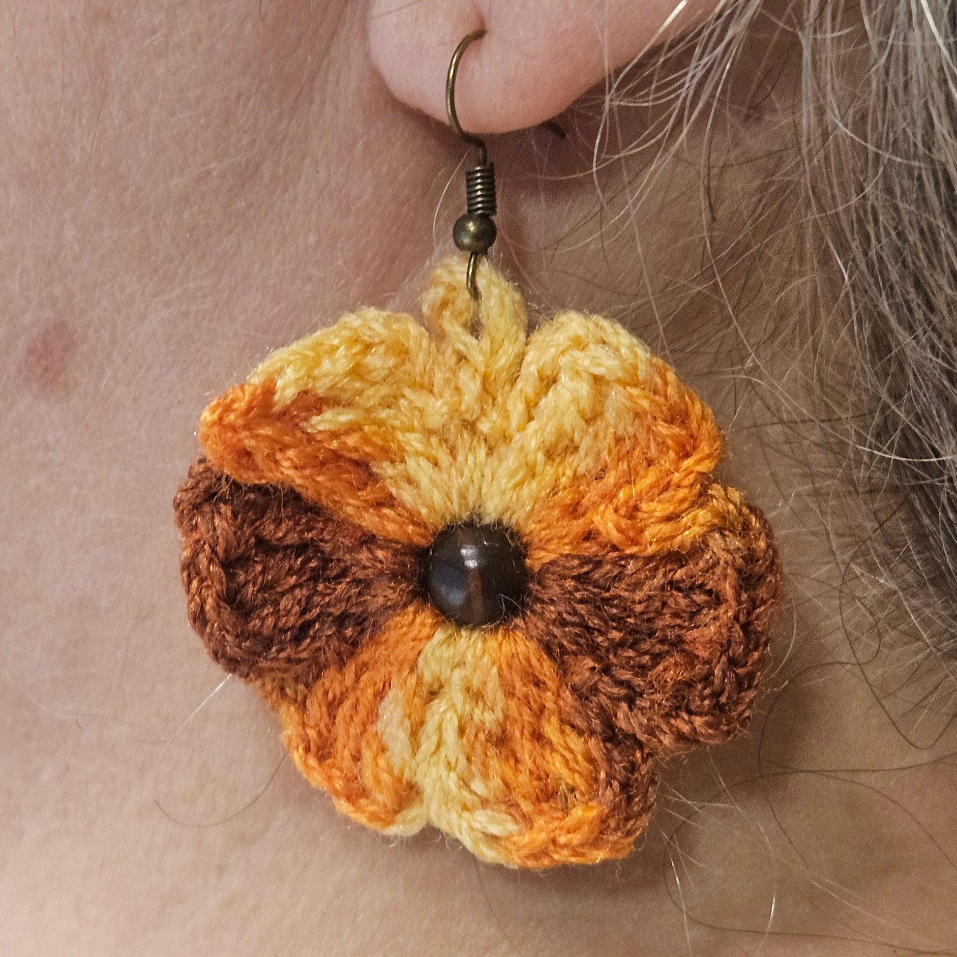 Crocheted flower earring worn on an ear with a neutral background