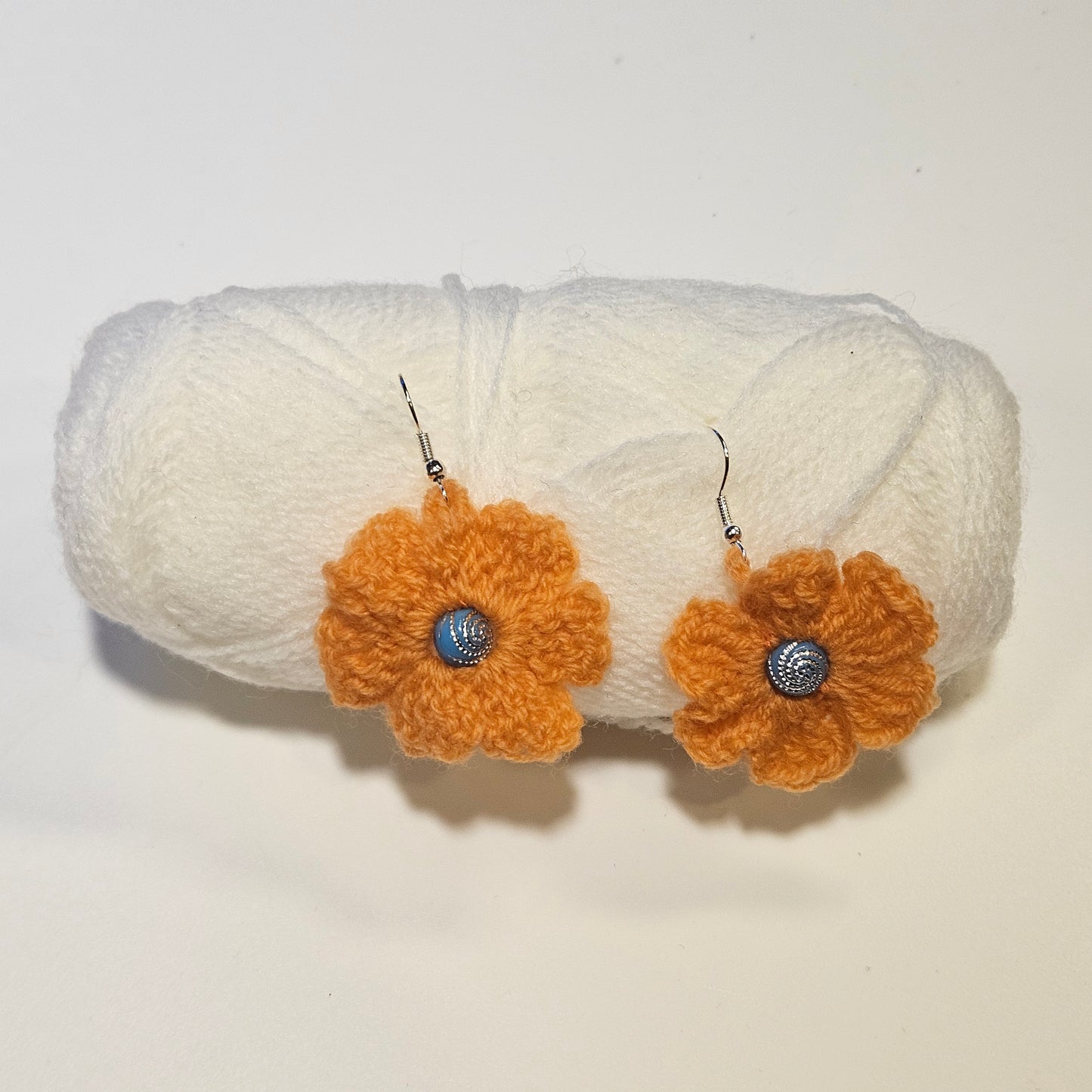 Pair of orange flower earrings with silver centers on a white background