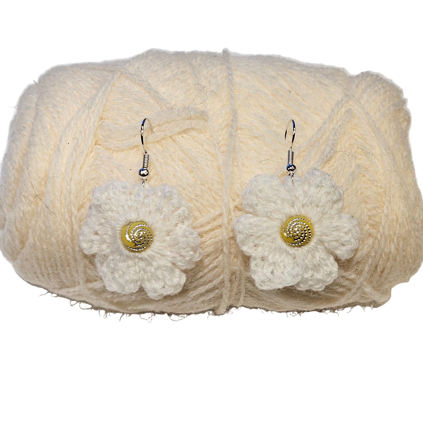 White crochet flower earrings with gold centers on a ball of cream yarn.