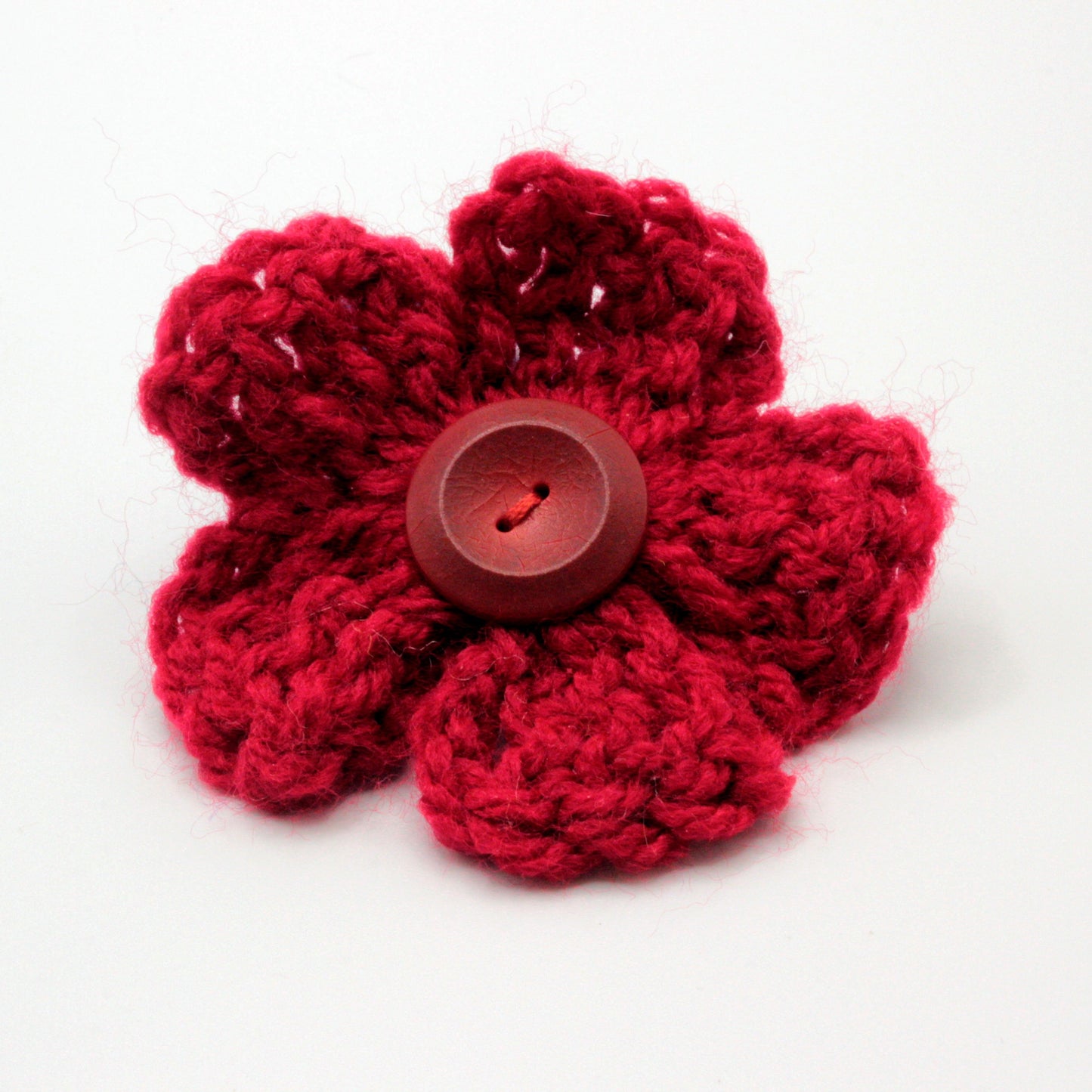 Red crocheted flower with a central button on a white background