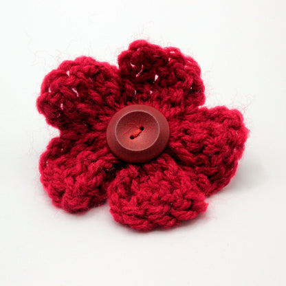 Red crocheted flower with a central button on a white background