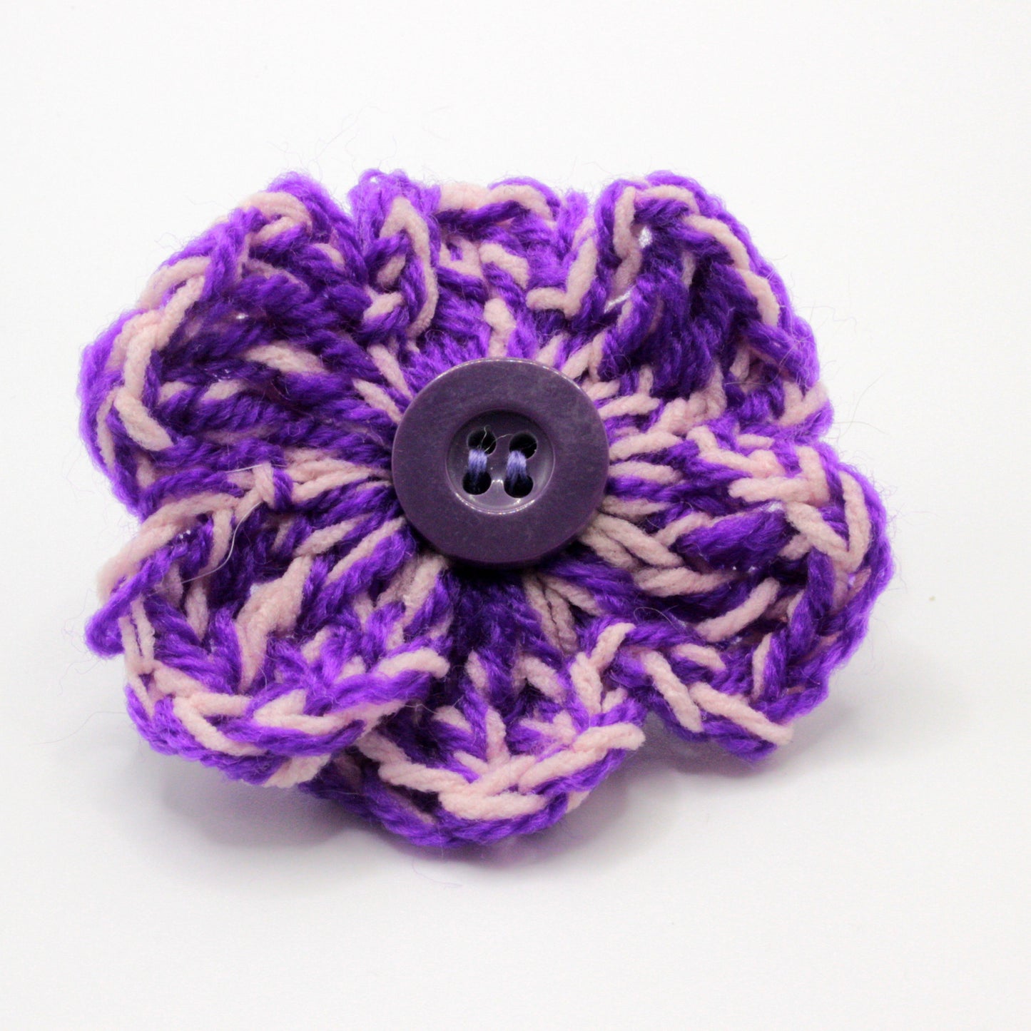 Purple and beige crocheted flower with a button center on a white background