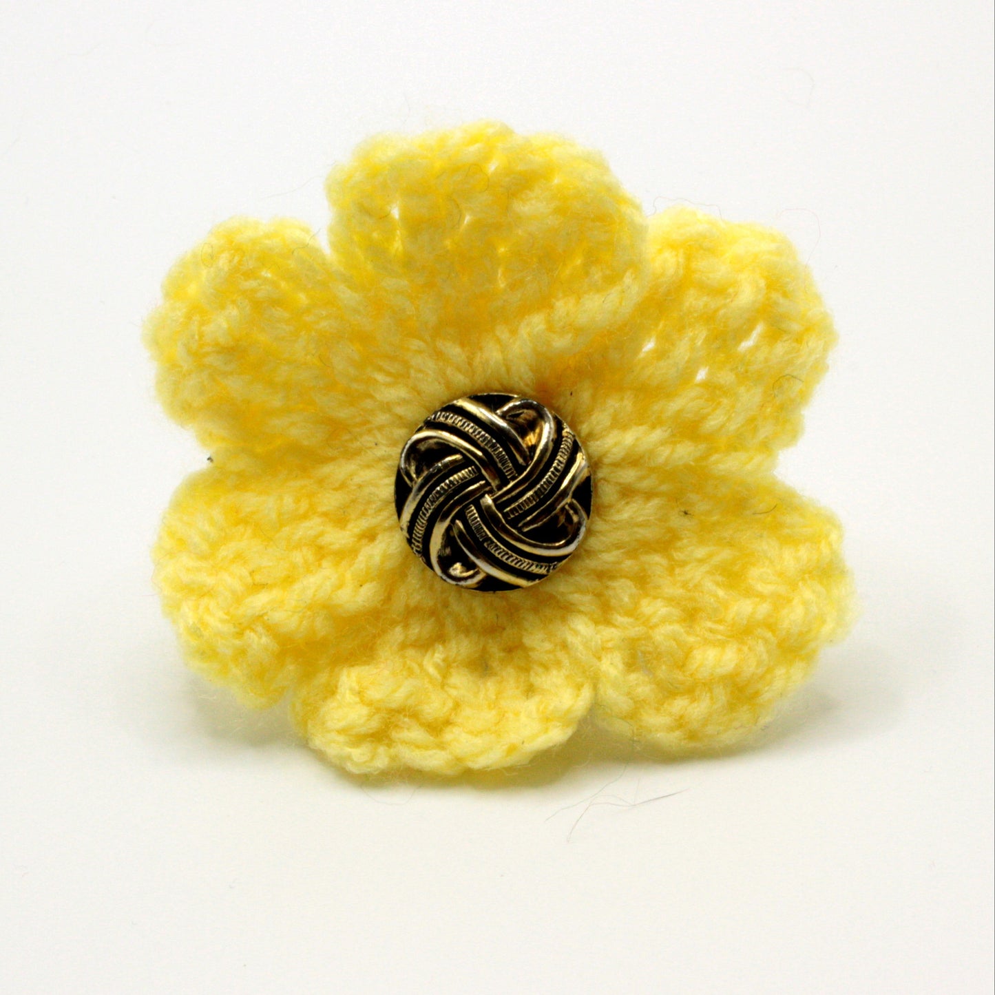 Yellow crocheted flower with a metallic center on a white background