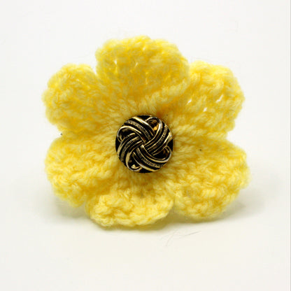 Yellow crocheted flower with a metallic center on a white background