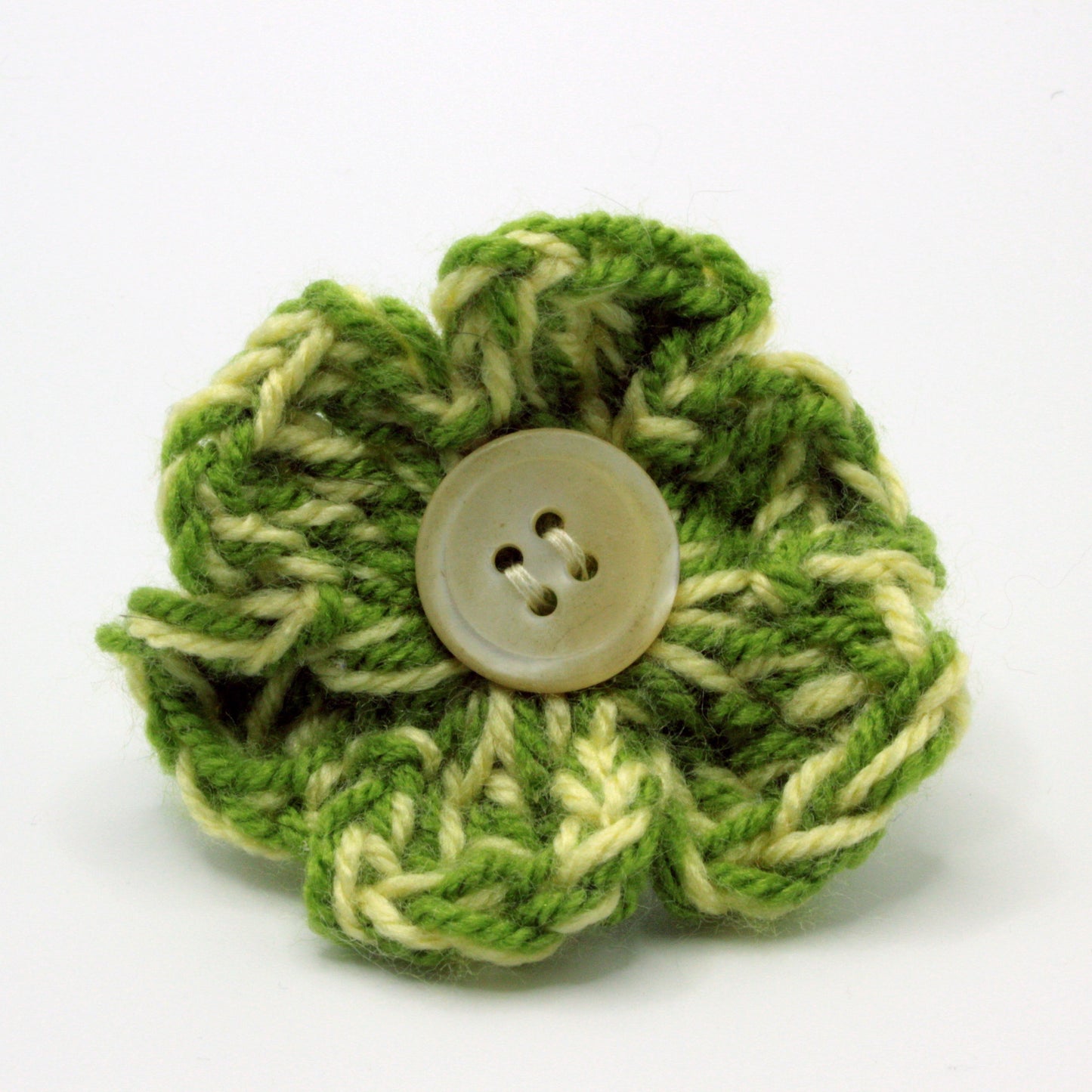 Green knitted flower with a button in the center on a white background