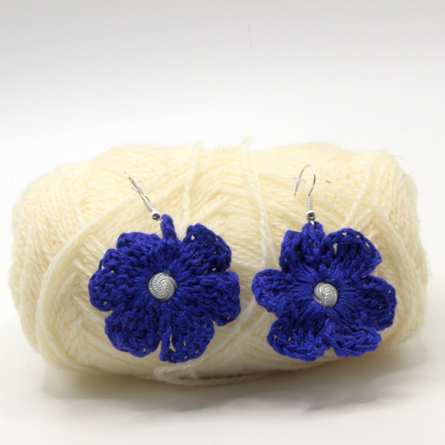 Blue flower earrings on a ball of yarn against a white background