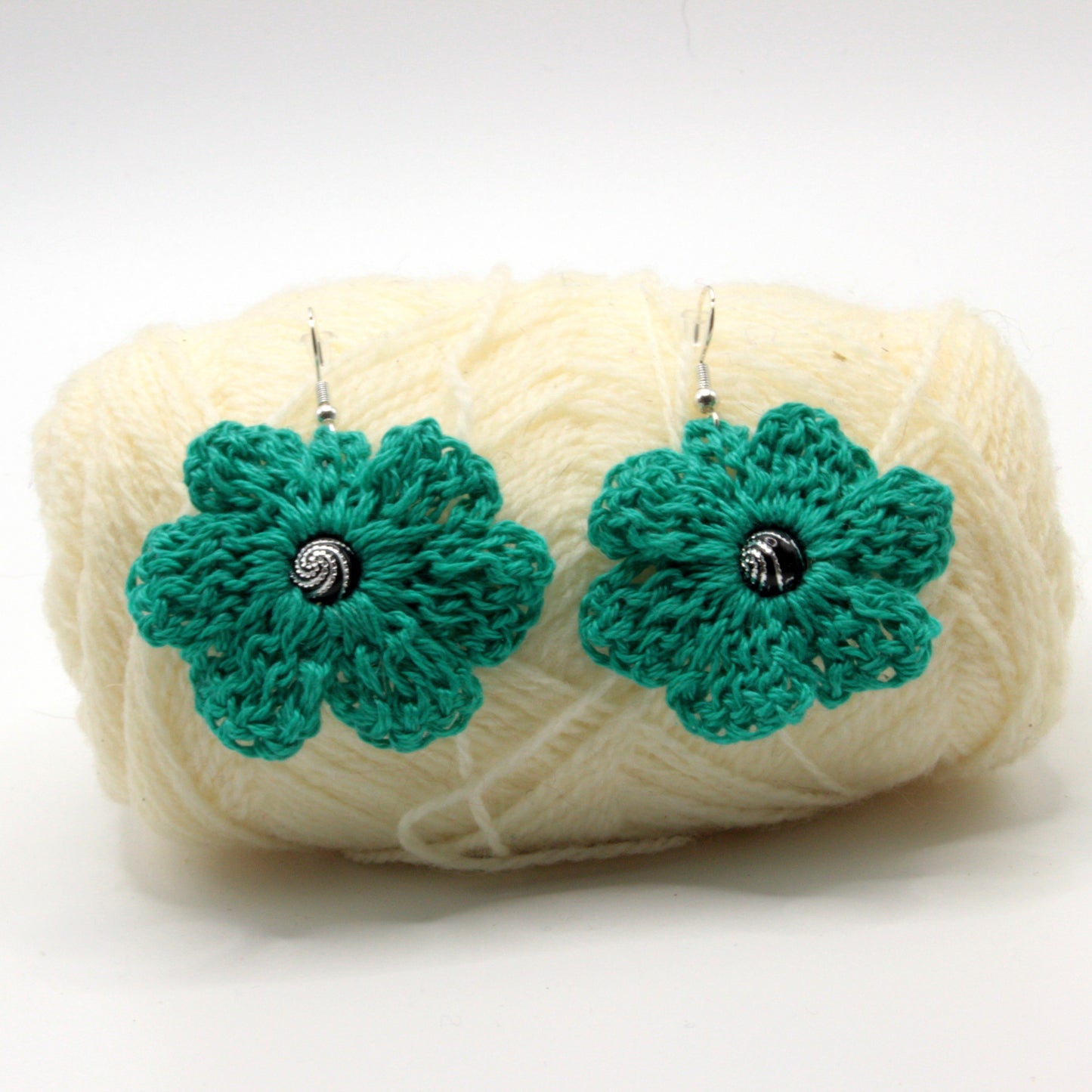 Green crocheted flower earrings on a ball of white yarn against a white background