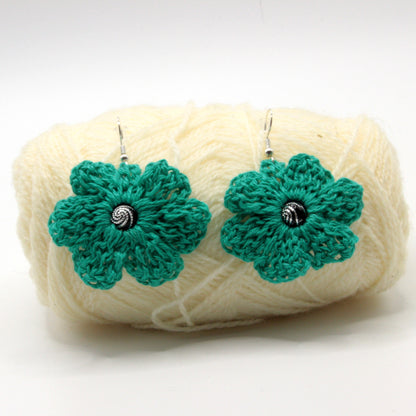 Green crocheted flower earrings on a ball of white yarn against a white background