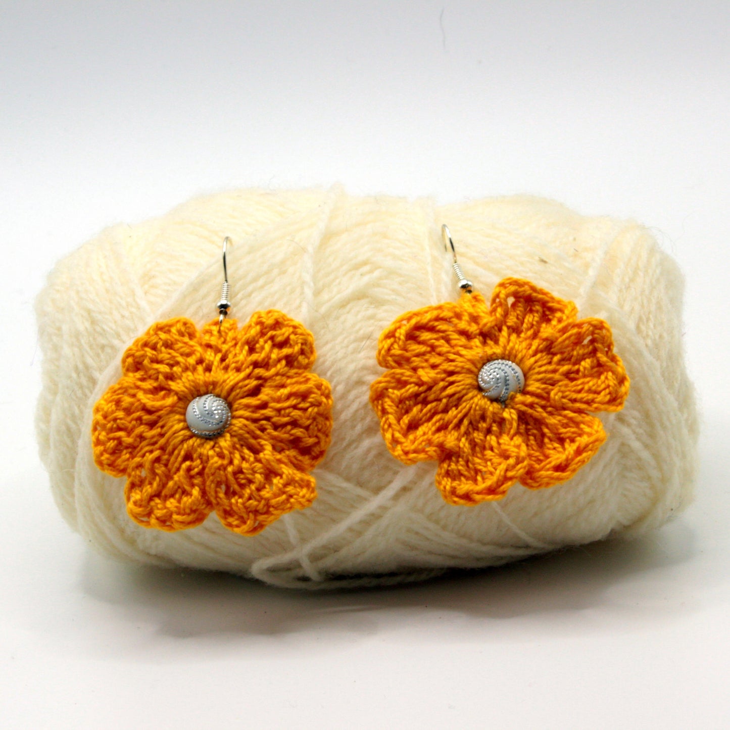 Orange flower earrings on a ball of yarn against a white background