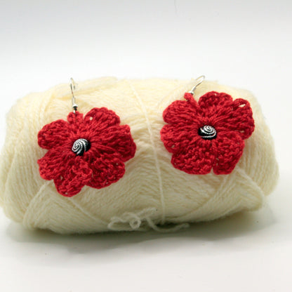 Yarn ball with red flower-shaped crochet earrings on a white background